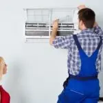 Air conditioning technician servicing a wall unit with a watching customer, from Atlantic Heating & Air Conditioning.