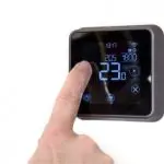 Digital thermostat with touchscreen showing 23.10°C, settings icons, time display, from Atlantic Heating & Air Conditioning.