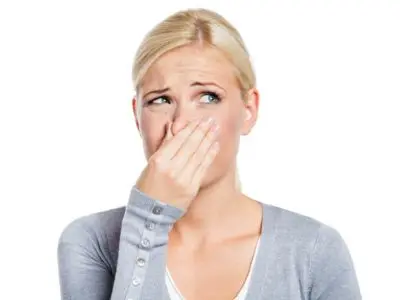 Woman covering her nose, reacting to bad odors, illustrating signs of air conditioning problems related to musty smells and potential mold growth.