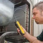 HVAC technician inspecting a refrigeration unit with a refrigerant leak detector for Atlantic Heating & Air Conditioning.