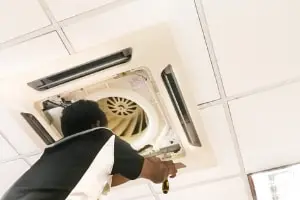 Technician servicing a ceiling-mounted HVAC unit, emphasizing maintenance for optimal home comfort.