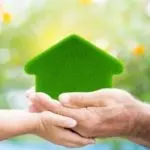Adult and child hands holding a green house symbol for eco-friendly HVAC solutions by Atlantic Heating & Air Conditioning.