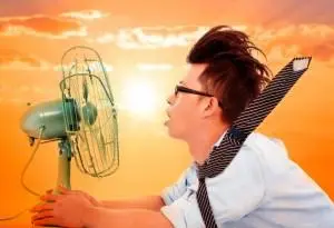 Person enjoying cool air from a vintage fan against a sunset backdrop, illustrating the importance of air conditioning for summer comfort.