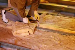 Person installing insulation in an attic to improve energy efficiency and prevent heating and cooling costs in a home.