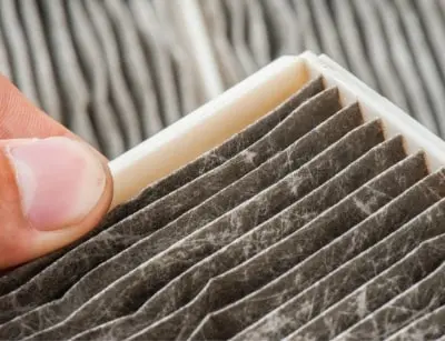 Close-up of a hand holding a dirty HVAC filter, illustrating the importance of regular filter changes for efficient heating and air quality in eco-friendly home heating systems.