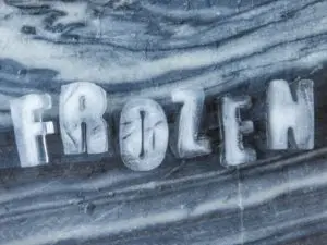 Ice letters spelling "FROZEN" on a textured surface, illustrating the concept of a frozen air conditioning unit as discussed in HVAC troubleshooting.