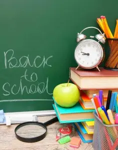 Back to school theme with a green chalkboard, clock, books, green apple, and colorful school supplies, symbolizing preparation for the upcoming school year.