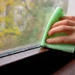 Hand cleaning a window with a green cloth, highlighting the importance of air quality and cleanliness for homes.