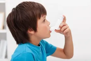 Boy using an asthma inhaler, highlighting respiratory health concerns related to dirty air conditioning systems and their impact on allergies and asthma.