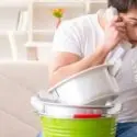 A man on the phone in a kitchen, multitasking with buckets and a mixing bowl for plumbing emergencies by Super Plumbers.