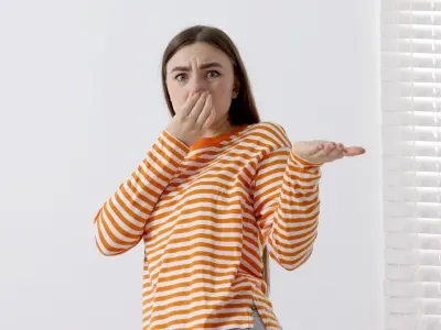 Person in striped orange and white shirt covering nose with one hand and gesturing with the other, expressing concern about a strong burning odor, indicative of potential furnace overheating issues.