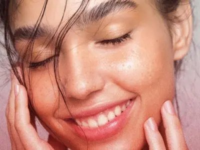 Smiling woman with glowing skin touching her face, illustrating skincare benefits related to moisture and hydration.