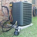 Air conditioning unit on a concrete platform with hoses, surrounded by grass and walls, by North Point HVAC services.