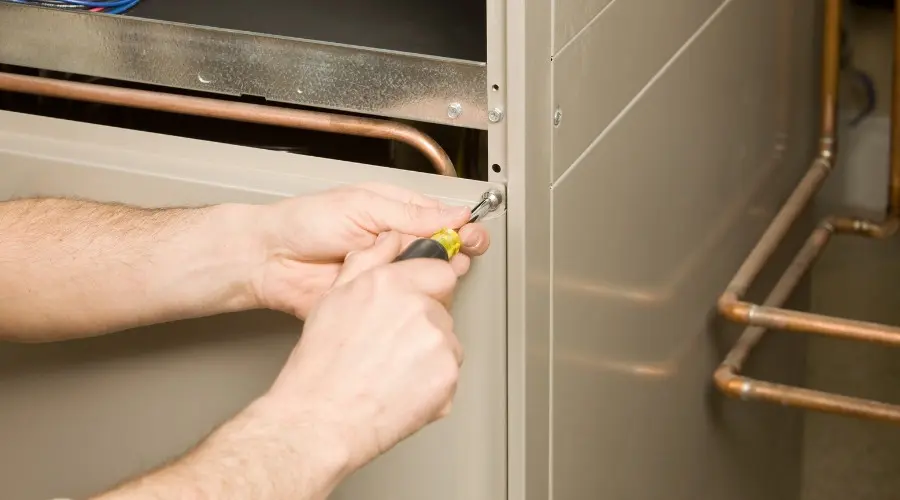 Technician performing maintenance on a heating system, using a screwdriver to secure a panel, emphasizing the importance of annual heating maintenance for efficiency and reliability.