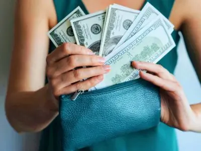 Person holding a teal wallet filled with cash, symbolizing savings and financial efficiency related to energy-efficient air conditioning maintenance.