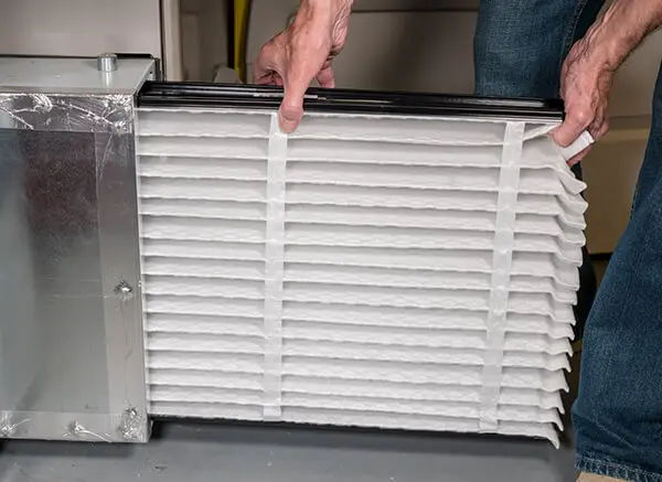 Person replacing a clean HVAC furnace filter, emphasizing maintenance for optimal airflow and winter preparation.