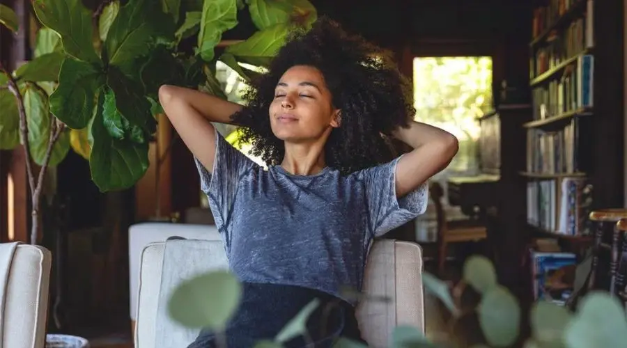 Woman relaxing indoors with closed eyes, surrounded by indoor plants, illustrating comfort and improved indoor air quality related to HVAC services.