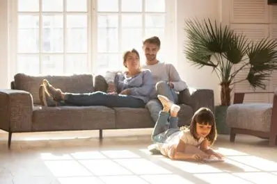 Family relaxing on a couch in a bright living room, with a child playing on the floor, emphasizing home comfort and family life during HVAC service wait times.