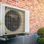 Wall-mounted air conditioning unit against a brick wall, surrounded by shrubbery for North Point Air Conditioning & Heating.