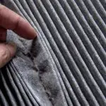 Close-up of a hand holding textured fabric, showcasing intricate pleats and grooves, emphasizing textile quality and design.