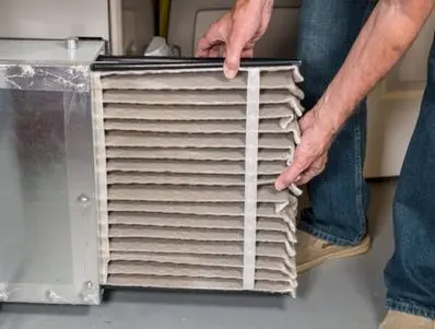 Person replacing a dirty HVAC filter in a heating system, illustrating the importance of regular maintenance for indoor air quality and efficient HVAC performance.