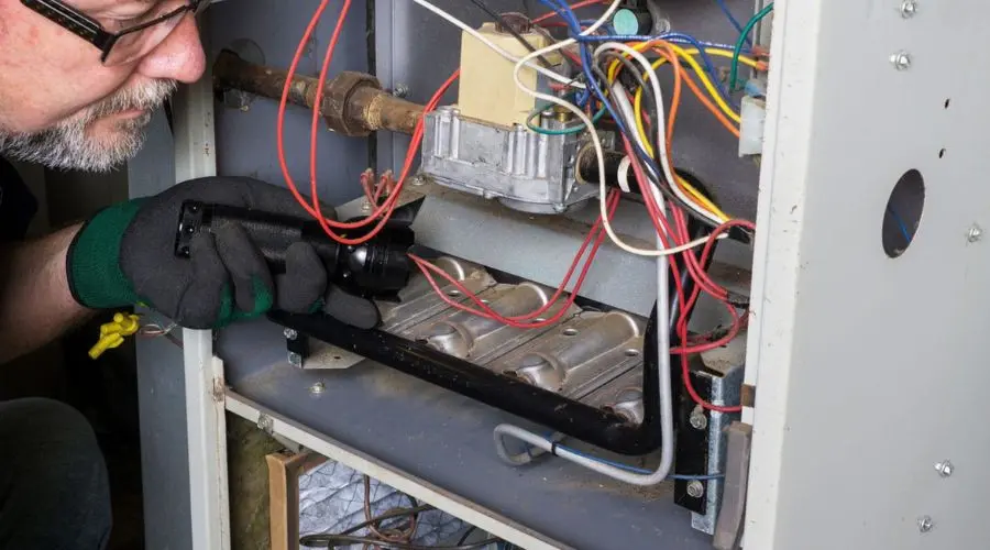 Technician inspecting heating unit components with flashlight, showcasing HVAC maintenance at North Point Air Conditioning.