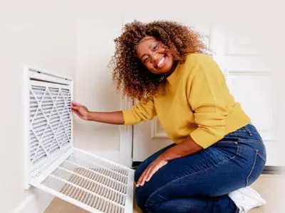 Woman smiling while replacing an air filter in a home, emphasizing the importance of regular air filter maintenance for improved indoor air quality and allergy relief.