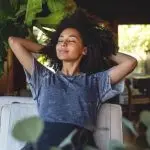 Young woman with curly hair relaxing indoors among plants, showcasing comfort in space serviced by North Point HVAC.