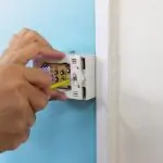 Hand installing a smart thermostat on a wall, illustrating HVAC upgrade and energy efficiency benefits.