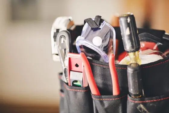 Tool belt filled with various tools including pliers, a level, and a tape measure, emphasizing the importance of maintenance for HVAC systems like furnaces.