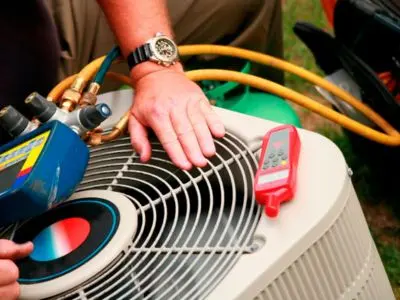 HVAC technician inspecting air conditioning unit with gauges and thermometer for routine maintenance and efficiency improvements.