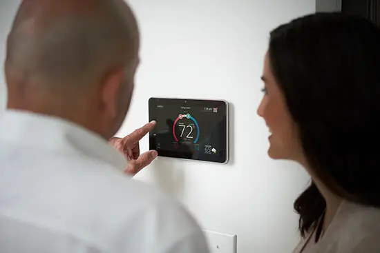 Couple adjusting a smart thermostat displaying 72°F, emphasizing home heating system management for winter preparedness.