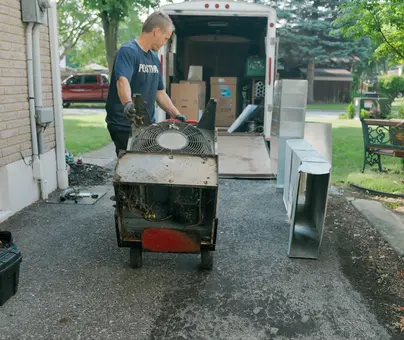 Postma HVAC technician removing an old air conditioning unit from a residential home during an AC replacement service in Chatham-Kent.