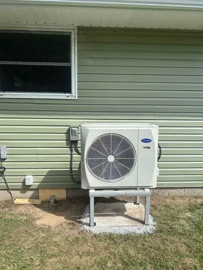 Carrier heat pump installed by Postma Heating, Cooling, Plumbing and Electrical on a raised stand outside a home in Chatham-Kent, Ontario.