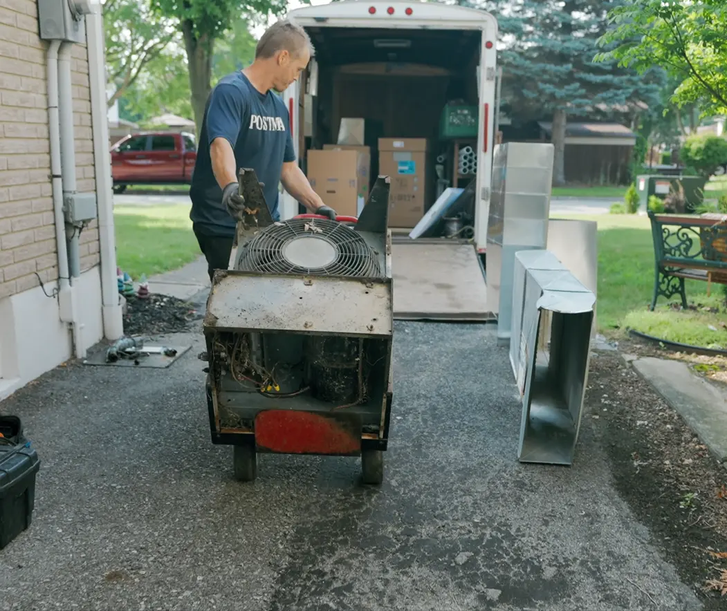 Postma HVAC technician removing an old air conditioning unit from a residential home during an AC replacement service in Chatham-Kent.