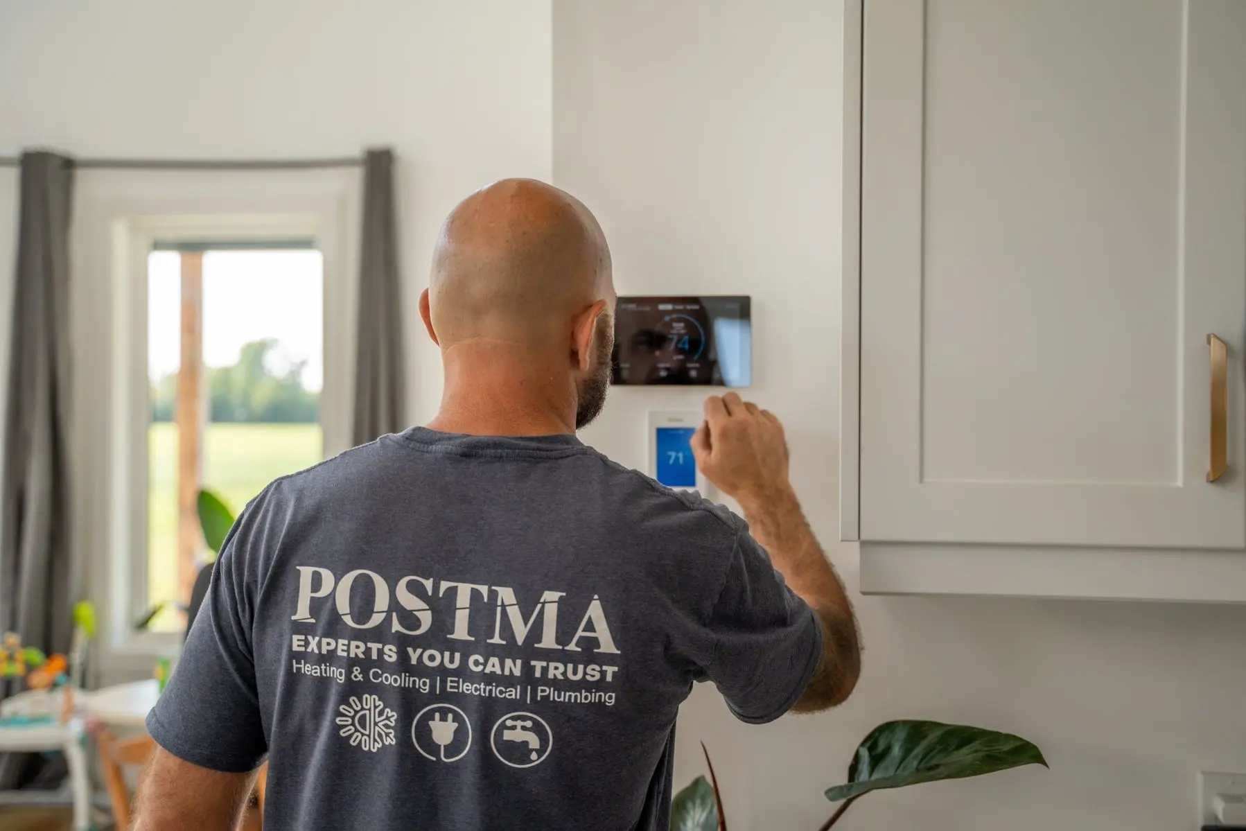 Postma HVAC technician in Chatham-Kent programming a smart thermostat to resolve heating and cooling issues and improve home energy efficiency.