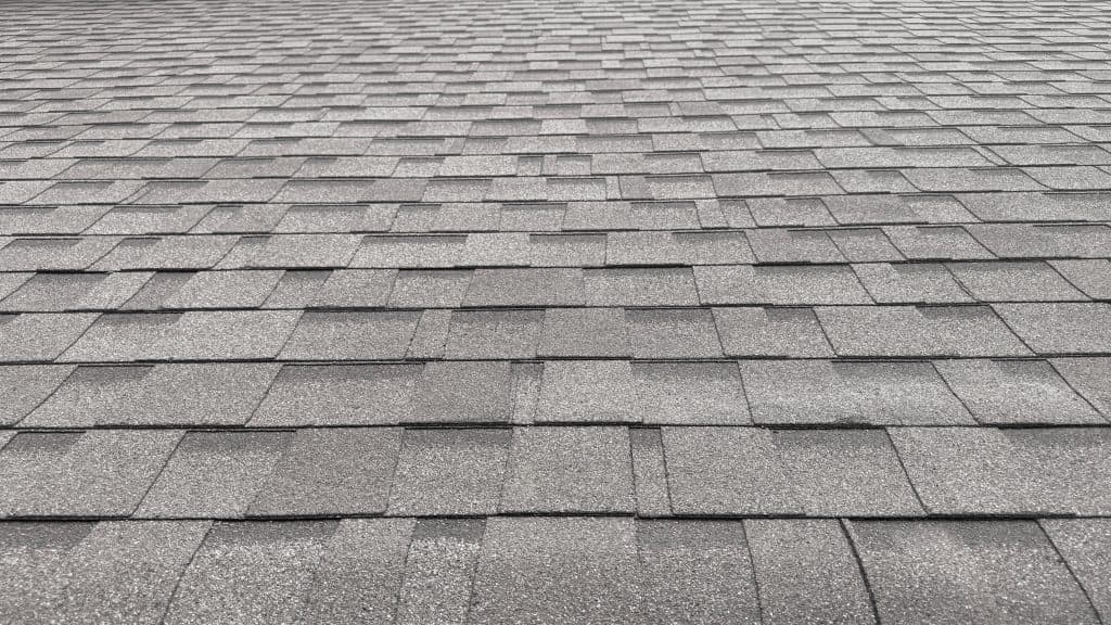 A close-up view of a gray asphalt shingle roof, showing the repeating rectangular pattern and textured surface from a low angle.