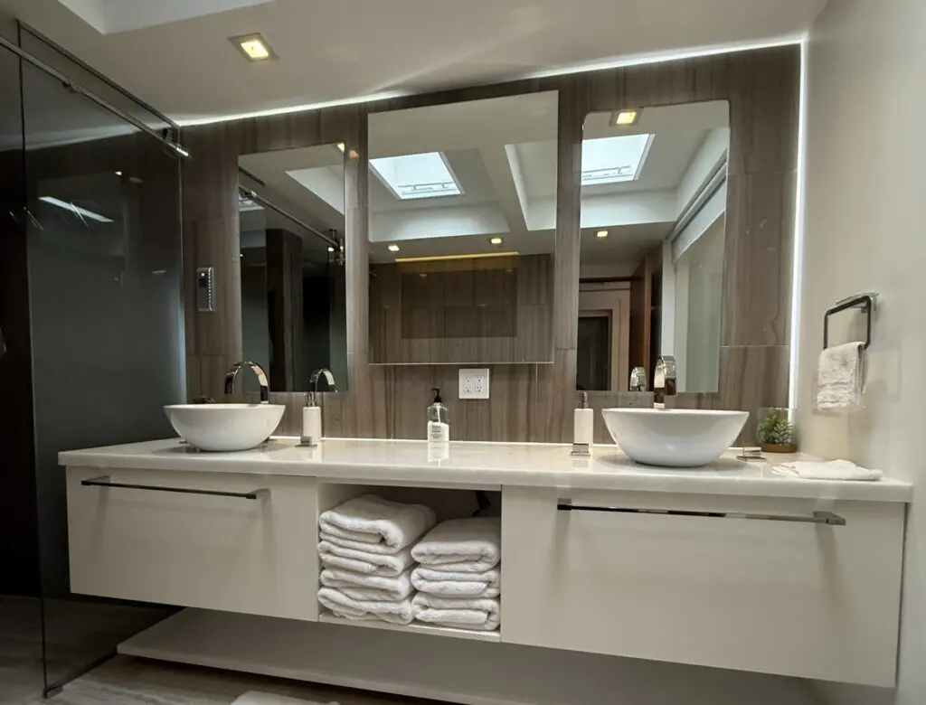 A wide floating vanity with two sinks, spotlights in the ceiling and two large mirrors