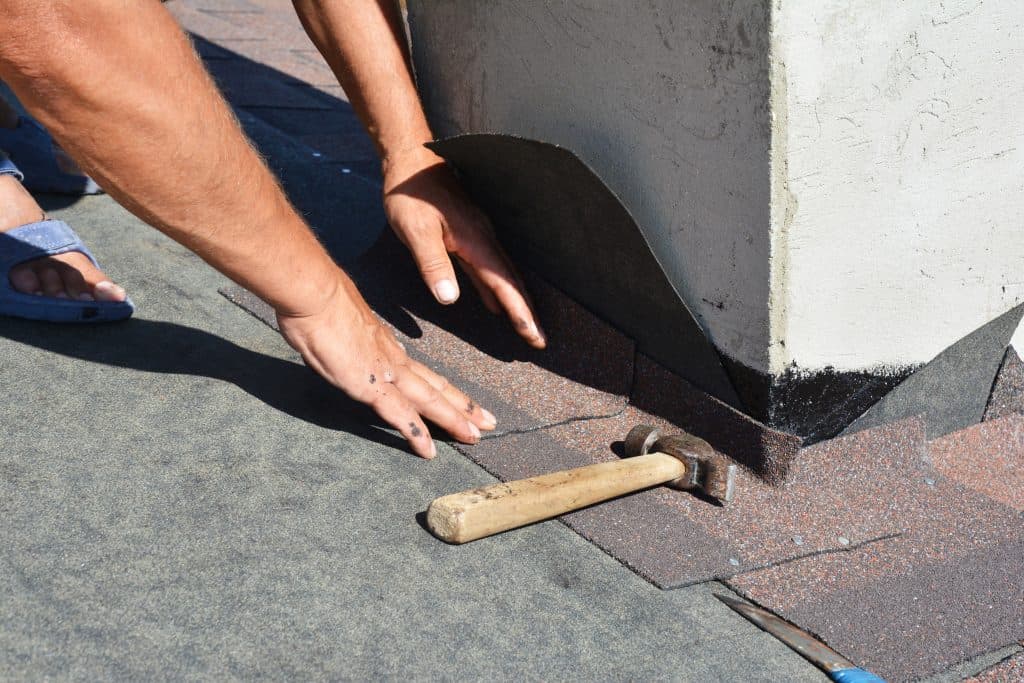 roof flashing repair Asphalt shingles roofing construction. Roofer repair and laying asphalt shingles with vapor barrier in chimney problem area. Chimney waterproofing on house rooftop.