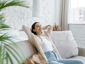 Woman relaxing on a sofa in a modern living room, enjoying comfort and tranquility, reflecting the benefits of efficient heating and cooling from heat pump systems.