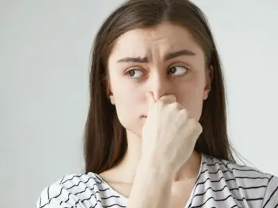 Woman holding her nose, expressing concern about unpleasant odors, relevant to air conditioning issues and maintenance.