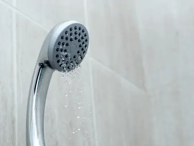 Showerhead with water flowing, illustrating potential causes of low water pressure from faulty fixtures or mineral buildup.