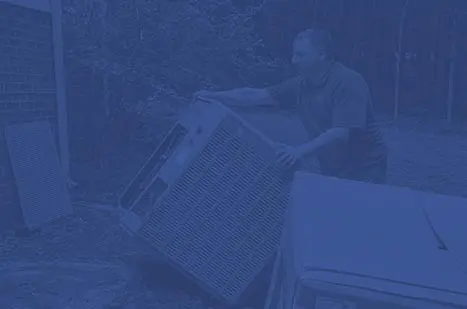 Technician removing an old air conditioning unit outdoors, emphasizing HVAC replacement services.