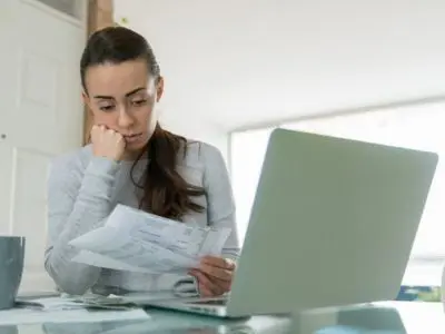 Woman reviewing increasing energy bills while using a laptop, reflecting concerns about HVAC efficiency and air conditioner maintenance.