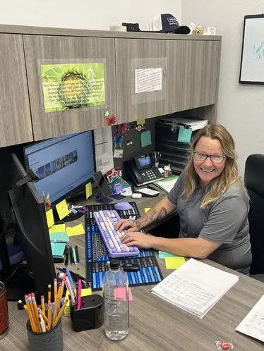 Woman working at a desk with a colorful keyboard, surrounded by office supplies and sticky notes, representing the support team at The Darville Company.