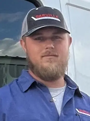 Young man in a cap, wearing a blue shirt, representing The Darville Company team outdoors with a vehicle in background.
