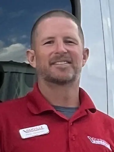 Smiling team member in red polo shirt with name tag, representing The Darville Company in a service environment.