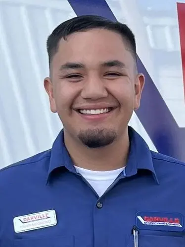 Young man in a blue shirt with name tags, representing The Darville Company team, smiling against a light background.