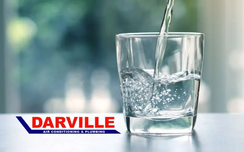 Clear glass filled with water, showcasing bubbles, with the Darville logo for plumbing and water quality services.