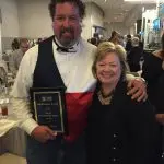Male and female individuals with an award plaque at a formal event for The Darville Company's achievements.